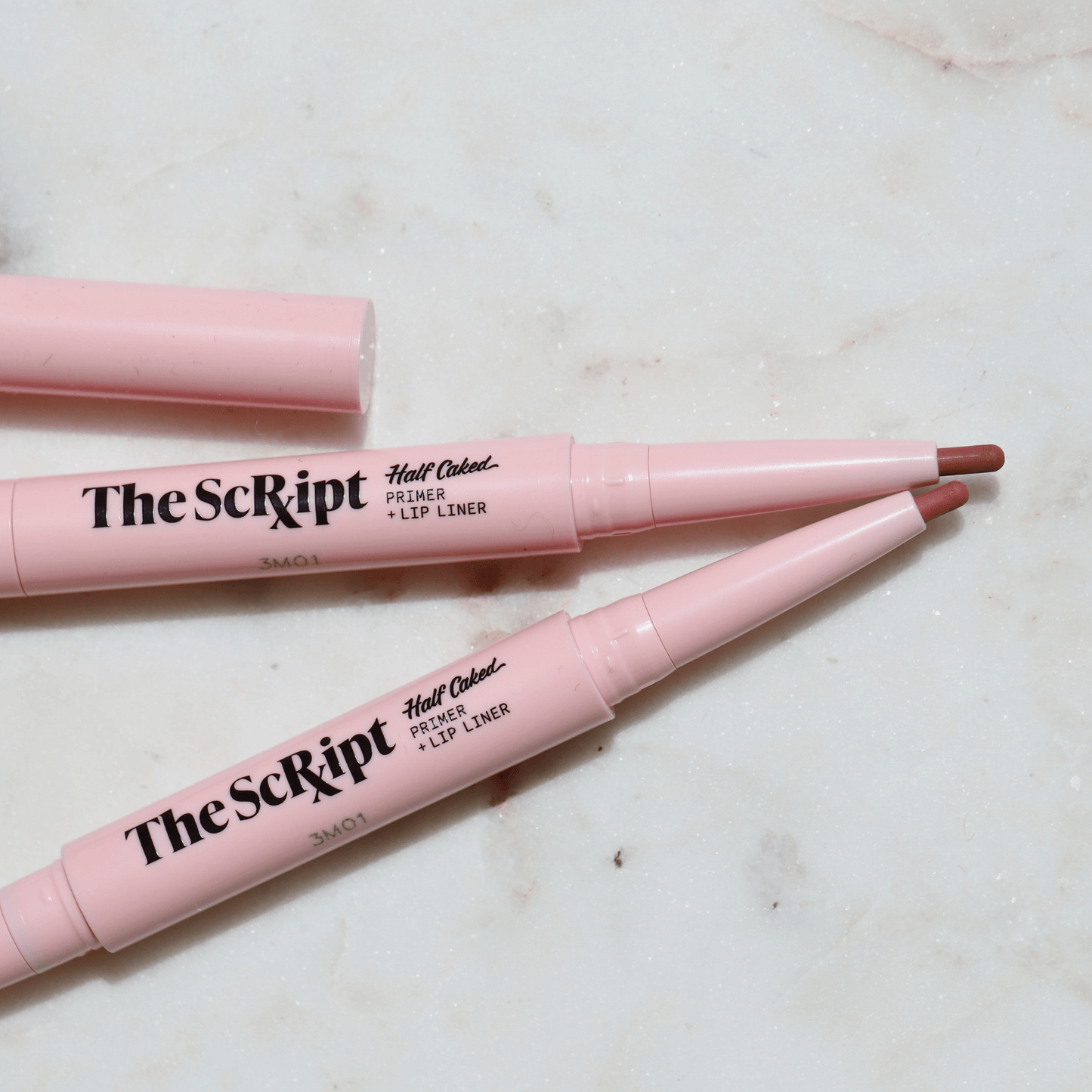 The Script Primer + Lip Liner, a dual-ended lip product with a primer and retractable lip liner, displayed on a marble surface.