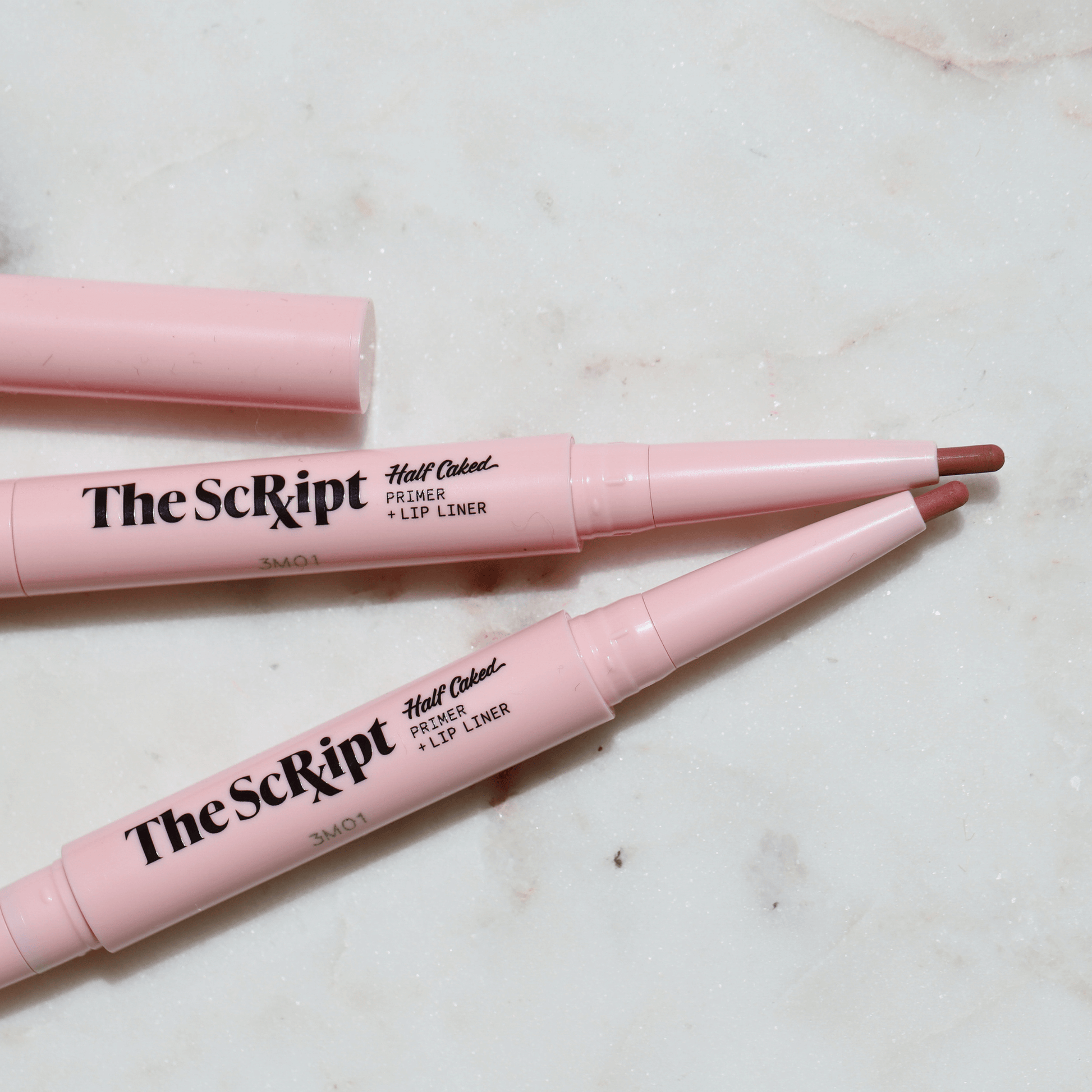 The Script Primer + Lip Liner, a dual-ended lip product with a primer and retractable lip liner, displayed on a marble surface.