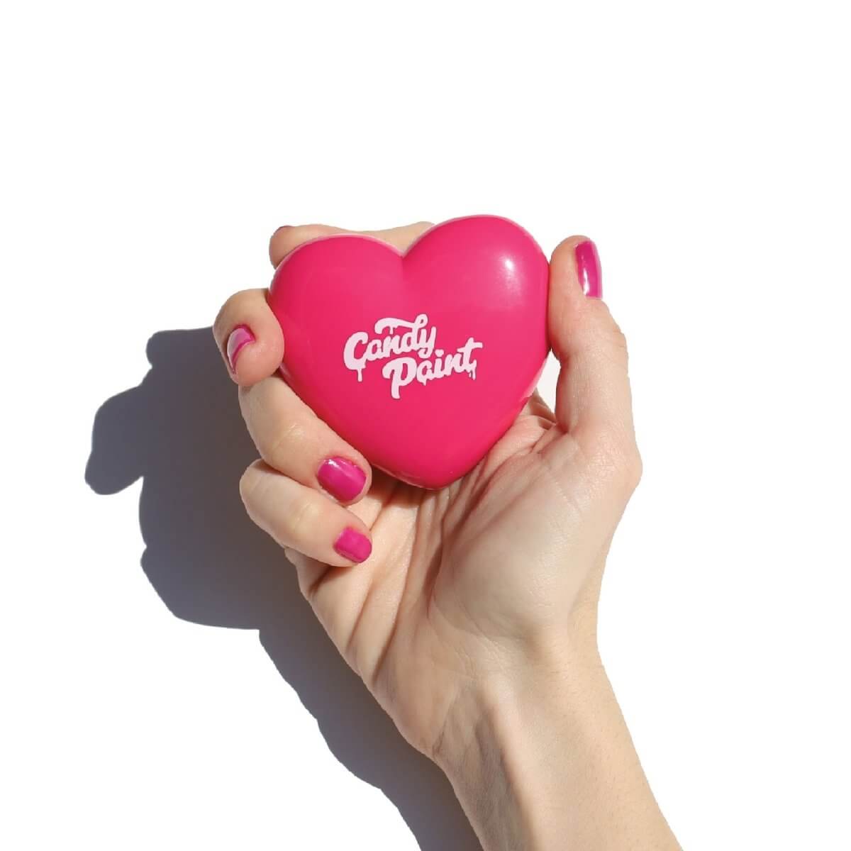 Hand holding a bright pink, heart-shaped compact labeled "Candy Paint".