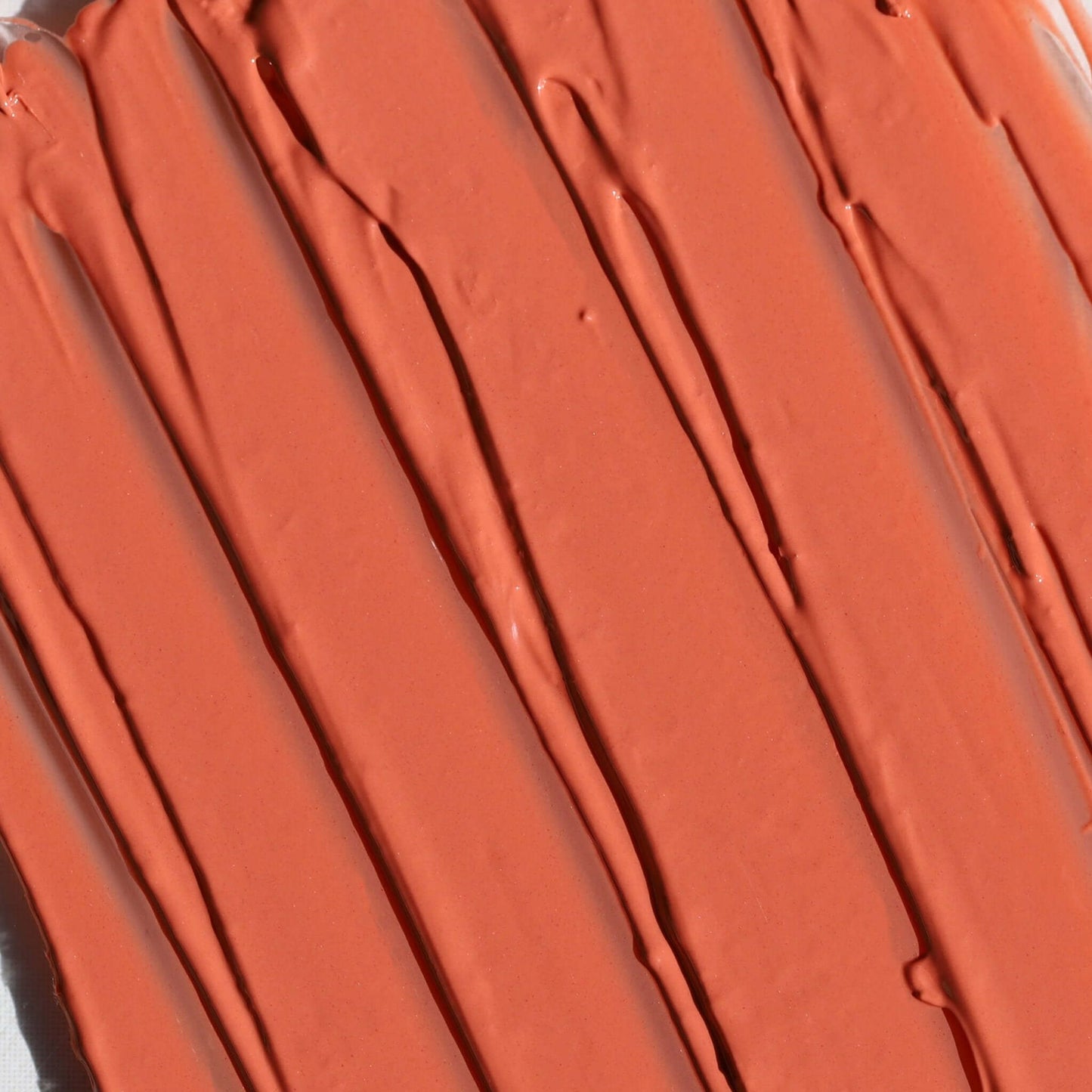 Close-up of the Candy Paint Cheek + Lip Tint texture in warm burnt orange, highlighting its creamy, blendable consistency for a radiant, dewy finish.